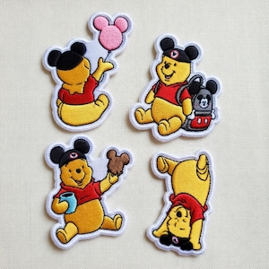 May include: Four embroidered patches featuring a yellow bear character in various poses. The bear wears a red shirt and a black hat with mouse ears. One patch shows the bear holding a pink balloon, another with a backpack, another with a treat, and another upside down.