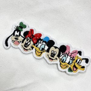 May include: Embroidered patch featuring the faces of Disney characters Goofy, Minnie Mouse, Donald Duck, Mickey Mouse, Daisy Duck, and Pluto. The patch has a white border and is designed with vibrant colors.