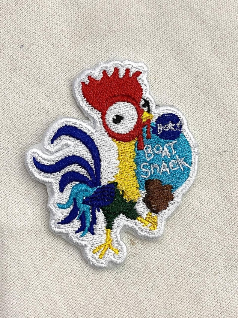 Pu&ograve; includere: Toppa ricamata raffigurante un gallo dei cartoni animati con cresta rossa, corpo giallo e penne della coda blu. Il gallo tiene in mano una borsa blu con la scritta "Boat Snack". La toppa ha un bordo bianco.