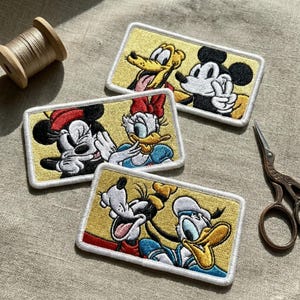 Può includere: Toppe ricamate con Topolino, Minnie, Paperino, Paperina e Pippo. Ogni toppa ha uno sfondo giallo con un bordo bianco. I personaggi sono in varie pose, con colori vivaci e cuciture dettagliate.