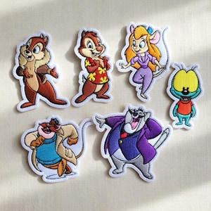 May include: A collection of seven embroidered patches showcasing cartoon characters. The patches feature colourful depictions of characters, including Chip and Dale, Gadget Hackwrench, and other figures from the animated series. Each patch has a white border.