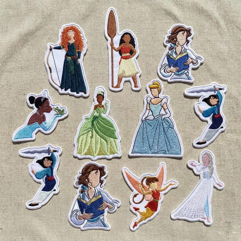 Op de afbeelding: Een verzameling geborduurde patches met verschillende geanimeerde vrouwelijke personages. De patches tonen gedetailleerde ontwerpen van personages, waaronder een prinses met pijl en boog, een prinses die een kikker vasthoudt en een prinses in een blauwe jurk. De patches hebben witte randen.