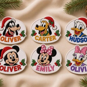 May include: Six oval embroidered patches featuring Disney characters wearing Santa hats and holly accents. The patches display the names Oliver, Carter, Hudson, Oliver, Emily, and Olivia in colorful embroidered lettering on a white background.