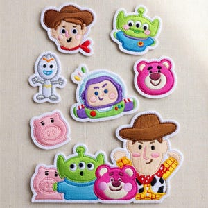 May include: A collection of embroidered fabric patches featuring characters from Toy Story, including Woody, Buzz Lightyear, an alien, Forky, Lotso, and Hamm. The set includes individual character heads and a larger group patch with multiple figures.