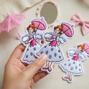 May include: Embroidered patches depicting a woman in a white dress with daisy details, holding a pink parasol. The patches have a white border and a whimsical design. A pink bow and miniature parasol are also present.