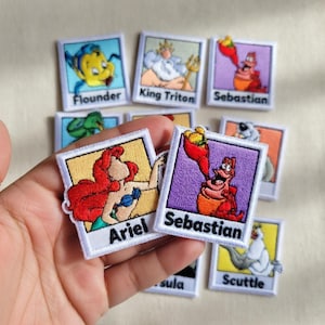 May include: A collection of embroidered patches featuring characters from the animated film "The Little Mermaid." Patches include Ariel, Flounder, Sebastian, King Triton, and Scuttle. Each patch has a white border and a character name.