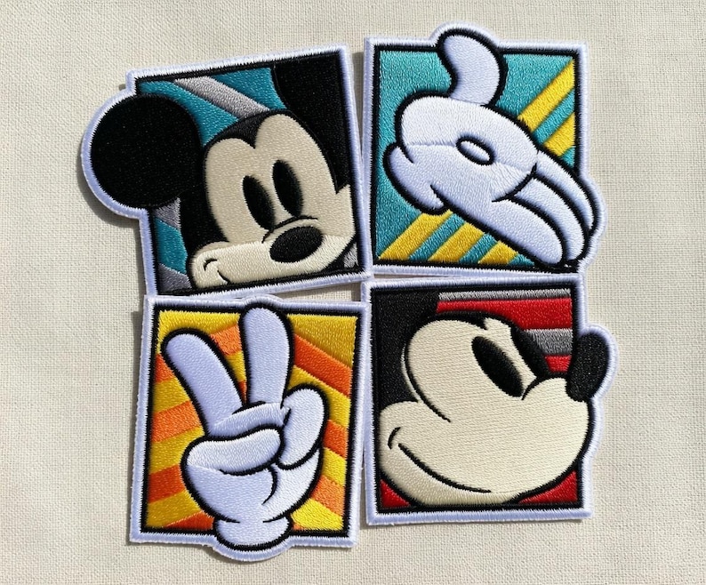 May include: Four embroidered patches featuring Mickey Mouse. One patch shows Mickey's face, two show his gloved hand, and one shows a peace sign. Each patch is square with a white border and colorful background.