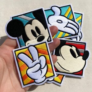 May include: A collection of embroidered patches featuring Mickey Mouse and his iconic imagery. Each patch is square with a colorful background, including a peace sign, a gloved hand, and Mickey's face. The patches are white, black, red, yellow, and blue.
