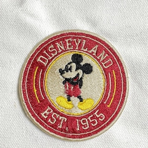 May include: Circular embroidered Disneyland patch with Mickey Mouse in red and white attire, yellow shoes, and black ears. The patch has a red border, with "DISNEYLAND" and "EST. 1955" embroidered on it.
