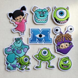 Peut inclure: Collection de patchs brodés représentant les personnages du film d'animation "Monstres et Cie". Comprend Boo en robe rose, Bob Razowski, Sulli et le logo Monsters, Inc. Les patchs ont des bordures blanches et sont posés sur un fond neutre.