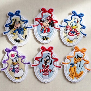 Puede incluir: Parches bordados con los personajes de Disney Mickey Mouse, Minnie Mouse, Pato Donald, Daisy, Goofy y Pluto. Cada parche tiene forma ovalada con un borde festoneado, una cinta y un lazo en la parte superior. Los personajes visten varios atuendos.