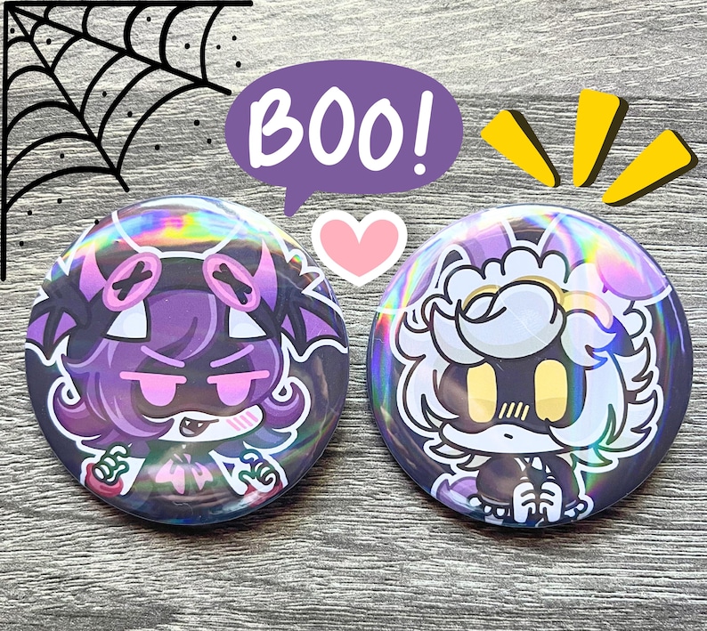 May include: Two round, holographic buttons with cartoon characters. One button features a purple character with pink accents, the other a white and yellow character. A purple speech bubble says "BOO!" with a pink heart and yellow accents.