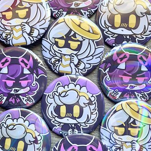May include: A collection of round, colorful buttons featuring anime-style character designs. The buttons showcase characters with white, purple, and black color schemes, with details like halos, wings, and stylized facial expressions. The buttons are arranged closely together.