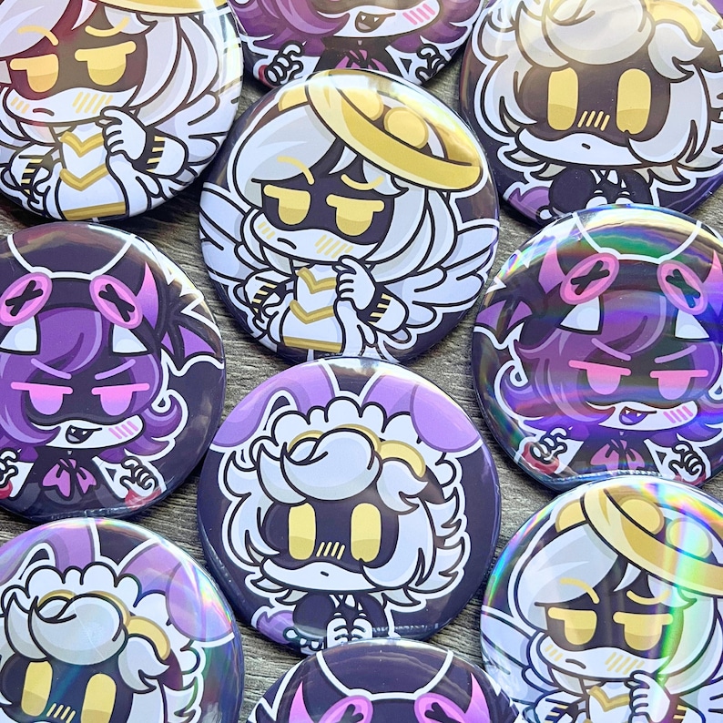 May include: A collection of round, colorful buttons featuring anime-style character designs. The buttons showcase characters with white, purple, and black color schemes, with details like halos, wings, and stylized facial expressions. The buttons are arranged closely together.