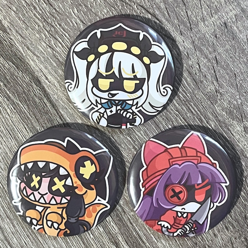 May include: Three round black buttons with colorful anime-style character designs. One features a white-haired character with a black and white outfit. Another shows an orange dinosaur-like character. The third button has a purple-haired character with a red outfit.