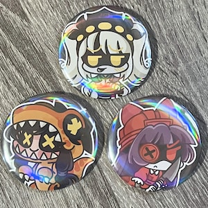 May include: Three holographic round buttons with cartoon character designs. The buttons feature characters with various expressions and outfits, including a dinosaur, a character with a knife, and a character with a crown.