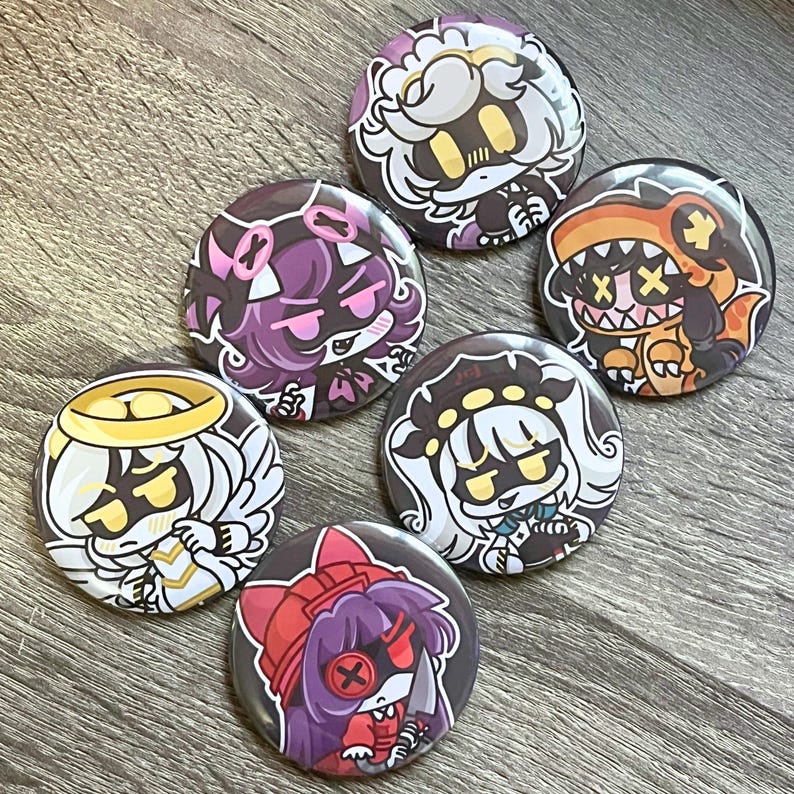 May include: A collection of seven round, colorful buttons with cartoon character designs. Each button features a different character with unique outfits and expressions, including an angel, a dinosaur, and a doll. The buttons are arranged on a wooden surface.