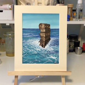 Puede incluir: Una pintura enmarcada de una alta formación rocosa marrón que emerge de un océano azul. El agua es de un color turquesa vibrante con espuma blanca alrededor de la base de la roca.