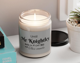 May include: A lit candle in a clear glass jar with a silver label. The label reads "Until Mr. Knightley Walks in, it's just Me and This candle". The candle is on a white surface.