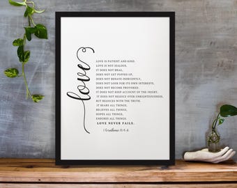 May include: Black framed print with the word "love" in cursive script and the text "Love is Patient and Kind" on a white background. The print is displayed on a wooden surface.
