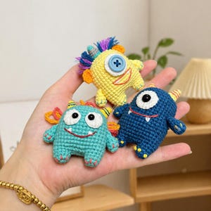 Peut inclure: Trois jouets monstres crochetés à la main en jaune, turquoise et bleu. Chaque monstre a un design unique avec des yeux en bouton, des sourires cousus et des accents colorés. Les jouets sont petits et semblent doux, parfaits pour les enfants.