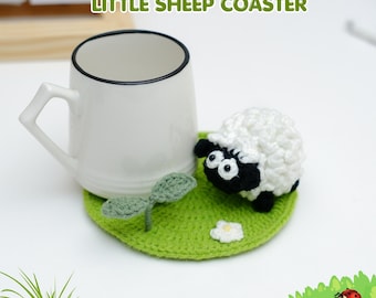 May include: A white ceramic mug with a black rim sits on a green crocheted coaster. The coaster features a crocheted sheep with a white body and black face. The coaster also has a crocheted leaf and flower. The text "PDF PATTERN LITTLE SHEEP COASTER" is visible.