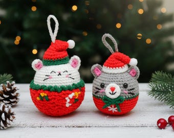 May include: Two crocheted Christmas ornaments shaped like mice. One is white with a red hat and the other is gray with a red hat. Both have a red base and green and white trim. The ornaments are decorated with festive details.