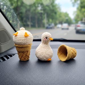 May include: A crochet set featuring a cream-colored ice cream scoop in a tan waffle cone, a small cream-colored duck figurine with orange beak and feet, and an empty tan crochet waffle cone, all crafted with visible yarn stitches.