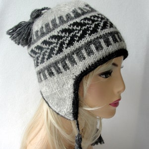 May include: A gray and black knitted winter hat with ear flaps and a pom-pom on top. The hat has a geometric pattern.