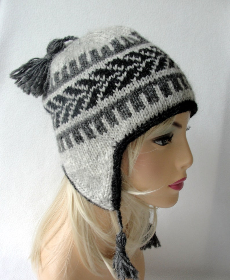 May include: A gray and black knitted winter hat with ear flaps and a pom-pom on top. The hat has a geometric pattern.