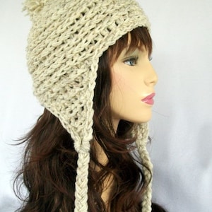 May include: A crocheted beanie with ear flaps and a pom pom on top. The beanie is made of a beige yarn and has a braided design on the ear flaps.