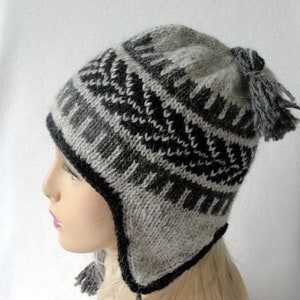 May include: A gray and black knitted winter hat with ear flaps and a pom-pom on top. The hat has a geometric pattern.