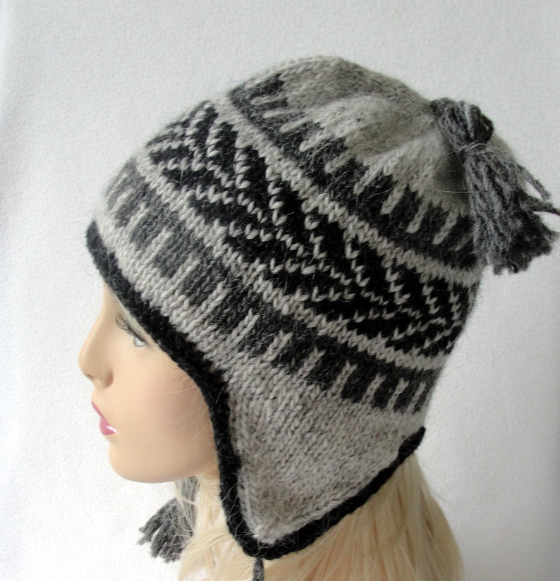 May include: A gray and black knitted winter hat with ear flaps and a pom-pom on top. The hat has a geometric pattern.