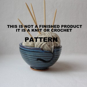 K&ouml;nnte beinhalten: Eine blaue Keramik-Garn-Schale mit einem wei&szlig;en Garnkn&auml;uel und Holzstricknadeln. Der Text "This is not a finished product it is a knit or crochet pattern" ist auf dem Bild gedruckt.