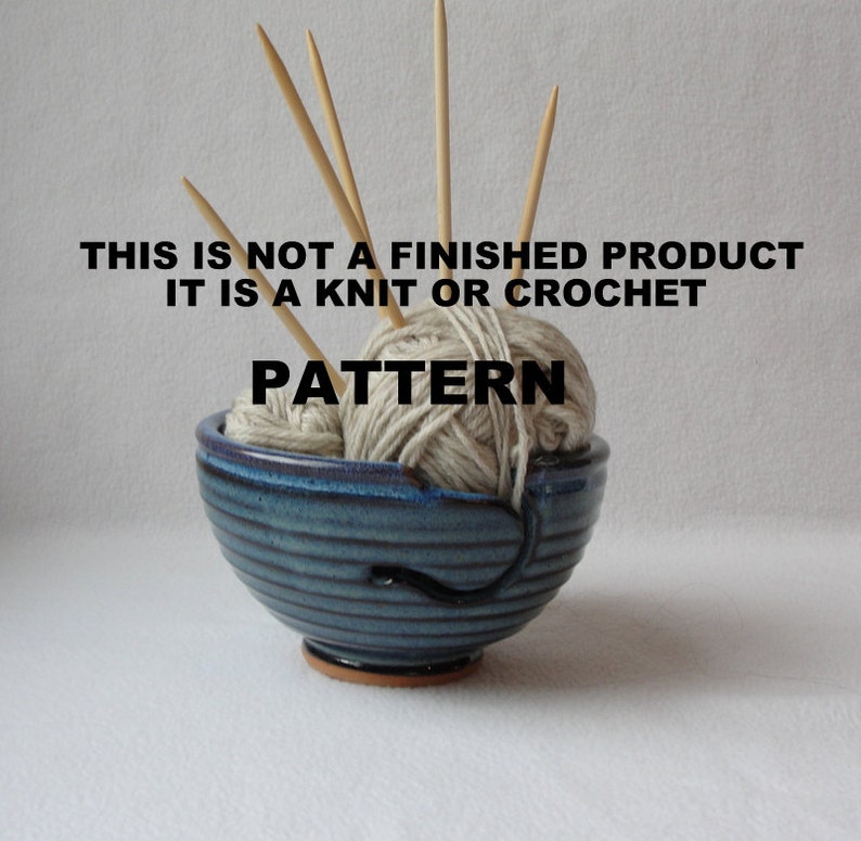 K&ouml;nnte beinhalten: Eine blaue Keramik-Garn-Schale mit einem wei&szlig;en Garnkn&auml;uel und Holzstricknadeln. Der Text "This is not a finished product it is a knit or crochet pattern" ist auf dem Bild gedruckt.