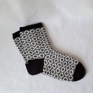 Può includere: Un paio di calzini a motivi neri e bianchi con un design geometrico. I calzini sono realizzati in un tessuto morbido e lavorato a maglia.