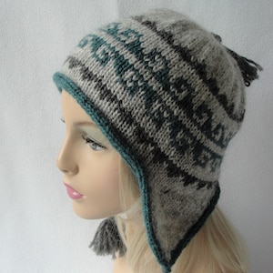 May include: A grey and teal knitted hat with ear flaps and tassels. The hat has a geometric pattern.