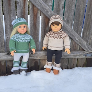 May include: Two dolls wearing matching knitted outfits. One doll is in a green sweater, hat, and leg warmers with white and light green patterns. The other doll is in a beige sweater, hat, and leg warmers with brown patterns. Both dolls are standing in the snow.