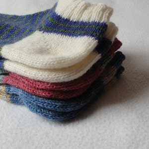 Pode incluir: Uma pilha de meias de malha coloridas. As meias apresentam várias combinações de cores, incluindo azul com listras verdes, branco, vermelho e cinza com detalhes em amarelo. As meias são feitas de um material macio e texturizado.