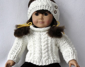 May include: White knitted doll sweater with a cable knit pattern and a turtleneck. The sweater has brown fur pom-poms on the sleeves and a white headband with two brown buttons.