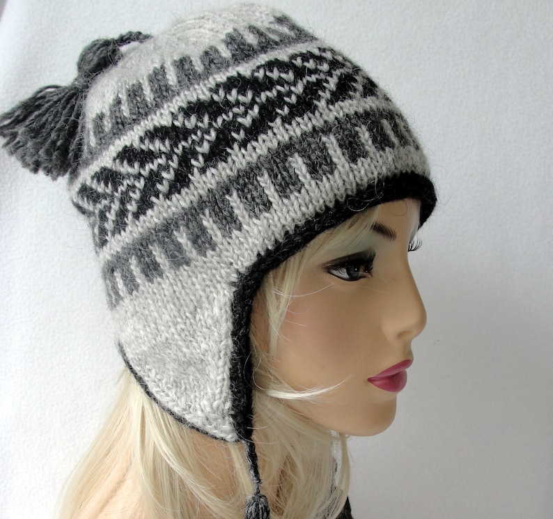 May include: A gray and black knit hat with ear flaps and a pom-pom on top. The hat has a geometric pattern.