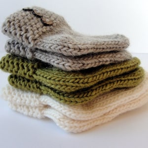 May include: A stack of four knitted fingerless gloves in different colors: beige, green, and white. The gloves are made with a simple knit stitch and have a textured look.
