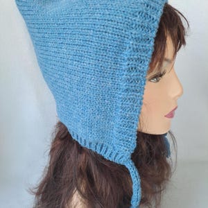 May include: A light blue knitted hat with a pointed top and ear flaps. The hat has a textured appearance and a tassel on each side. The hat is made of a soft, possibly wool, material.