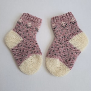 May include: A pair of pink and white knitted socks with a geometric pattern. The socks are made of a soft, warm yarn and are perfect for keeping your feet cozy in the winter.
