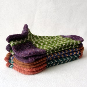 May include: A stack of four colourful knitted socks. The top sock is purple, green and white. The second sock is brown, orange and green. The third sock is blue, orange and green. The bottom sock is red, orange and green.