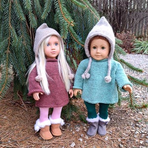 May include: Two dolls dressed in handmade knitted outfits. One doll wears a burgundy sweater dress, pink tights, and tan boots. The other doll is in a teal sweater, green leggings, and gray boots. Both dolls have matching knit hats.