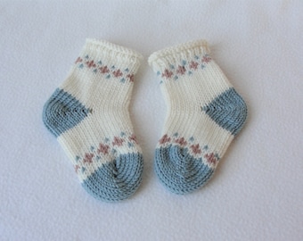 May include: A pair of knitted baby socks in white, blue, and pink with a geometric pattern.