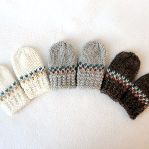 May include: Six knitted mittens in various colors: off-white, gray, and brown. Each pair features a decorative band with a geometric pattern in teal, gold, and other colors. The mittens are arranged in a semi-circle on a white surface.