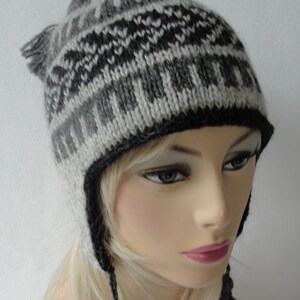 May include: A gray and black knitted hat with a geometric pattern. The hat has ear flaps and a long tie.