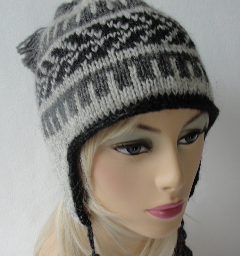May include: A gray and black knitted hat with a geometric pattern. The hat has ear flaps and a long tie.